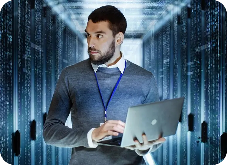 A man holding a laptop in front of some servers.